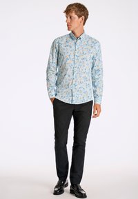 Ljusblå skjorta med knappar och blommönster i gult och grönt. Kombinerad med svarta byxor och blanka svarta skor.