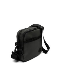 Juodas stačiakampis crossbody krepšys, pagamintas iš lygos, patvarios medžiagos. Turintis dvi užtraukiamas kišenes ir reguliuojamą dirželį.