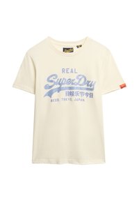 T-shirt en coton couleur crème avec un logo imprimé bleu "REAL SuperDry" et une petite étiquette rouge sur la manche. Manches courtes, col rond.