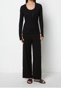 Czarny prążkowany kardigan z długimi rękawami i guzikami, w połączeniu z czarnym topem na ramiączkach i spodniami o szerokich nogawkach. Całość dopełniają czarne, płaskie sandały.