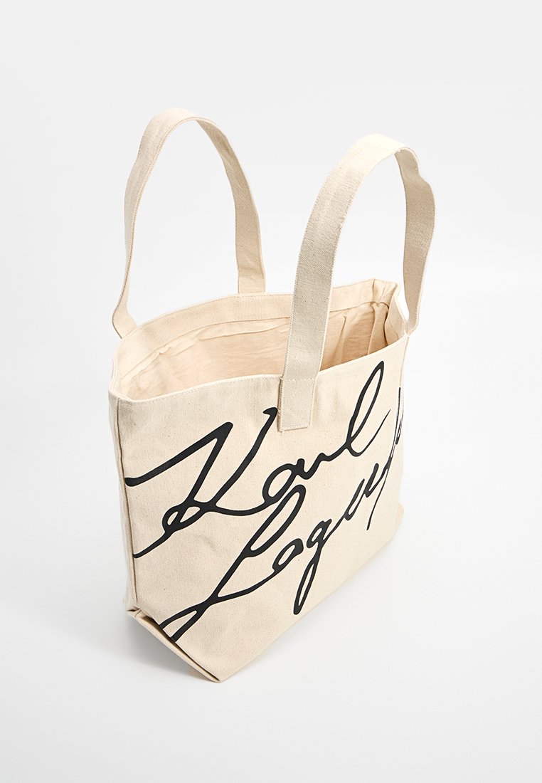 Sac en toile beige avec deux poignées et texte en cursive noir imprimé sur le devant.