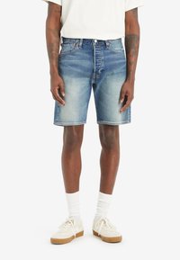 Shorts in denim blu chiaro con finitura sbiadita, design a cinque tasche e cuciture visibili. Indossati con una t-shirt bianca e sneakers color crema.