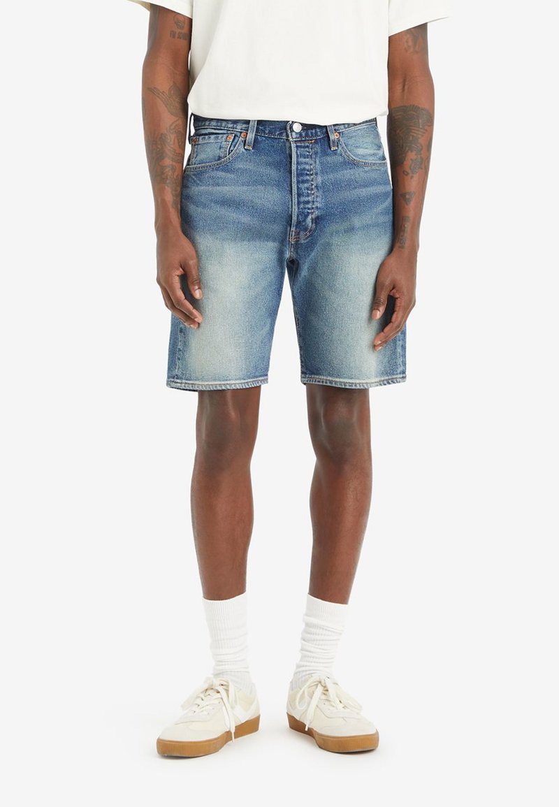 Shorts in denim blu chiaro con finitura sbiadita, design a cinque tasche e cuciture visibili. Indossati con una t-shirt bianca e sneakers color crema.