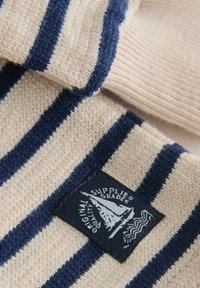 Tissu en maille beige avec des rayures bleu foncé et une étiquette noire arborant un voilier blanc et le texte « Original Quality Supplies Grade ».