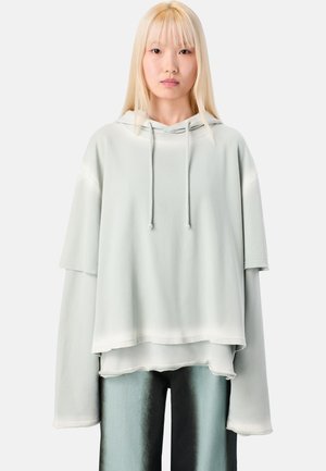 Hellgrüner oversized Kapuzenpullover mit Kordelzugkapuze, gestaffeltem Design und weit geschnittenen Ärmeln. Weicher Stoff mit leicht glänzender Textur.