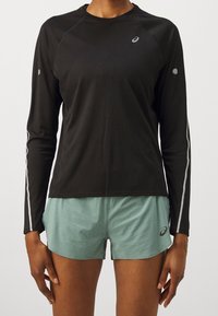Černé dlouhé rukávy sportovní tričko s šedými akcenty a raglánovými rukávy, v kombinaci se světle zelenými šortkami s vzorovanou texturou a božním logem.