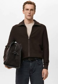 Brązowy sweter na zamek z dzianiny o fakturowanym wykończeniu, noszony na beżowej koszuli. W lewej ręce trzymane są czarne dżinsy oraz ciemna zamszowa torba.