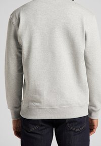 Szary sweter z okrągłym dekoltem, ribbowymi mankietami i dołem; gładka faktura i luźny fason; noszony z ciemnymi dżinsami.