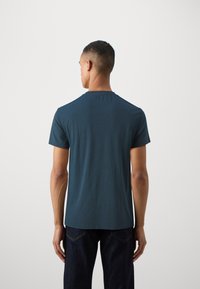 Short-sleeve, crew-neck t-shirt in dark blue fabric. Features a smooth texture and a relaxed fit. Visible stitching along the shoulder seams.