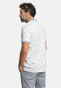 Polo de manga corta con base blanca, patrón floral en azul claro y cuello gris en contraste. Tejido de mezcla de algodón con un corte relajado.