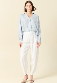 Blusa a righe blu chiaro con maniche lunghe, scollatura a V e chiusura con bottoni abbinata a pantaloni bianchi a vita alta e sandali con tacco metallici.