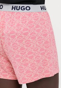 Pink boxer shorts with a textured white abstract pattern, featuring a grey elastic waistband with "HUGO" printed in navy.