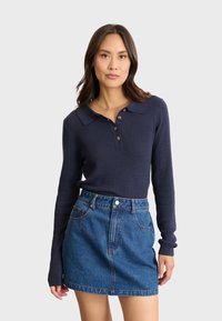 Marinblå ribbad långärmad polo med knäppning, kombinerad med en denimkjol. Har en klassisk krage och en figursydd silhuett.