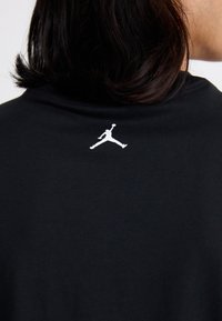 T-shirt en coton noir avec un logo blanc au dos, col rond et manches courtes, affichant une texture lisse.