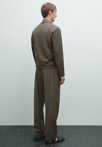 Khaki zielony komplet z kołnierzykową kurtką i luźnymi spodniami, wykonany z miękkiego materiału. Czarne sandały dopełniają look.