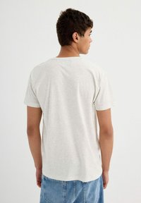Camiseta de algodón gris claro con cuello redondo y mangas cortas, con un corte relajado y una textura suave.