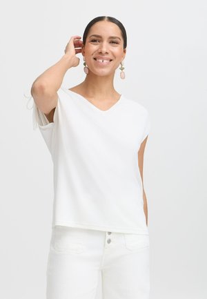 White V-neck top with short sleeves featuring decorative ties at the shoulders. Smooth fabric with a relaxed fit, paired with white trousers.