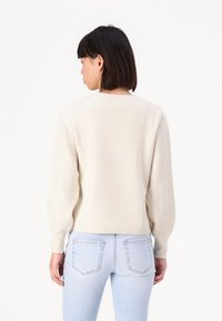 Light beige, knit sweater with a round neckline, long balloon sleeves, and ribbed hem. Worn with light blue jeans, featuring pockets.