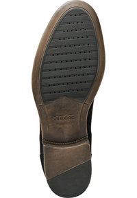 Sole di scarpa in pelle nera con un design texturizzato e scanalato, dotata di fori di ventilazione; presenta un accento marrone vicino al tallone con la scritta "GEOX" in rilievo.