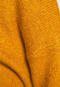 Stickad tröja i en livlig gul färg. Har en mjuk textur med en ribbad design och små variationer i garnets tjocklek genom hela plagget.