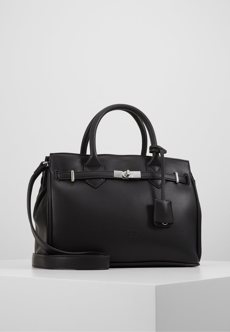 Sac à main en cuir noir avec doubles poignées, bandoulière amovible et fermoir tournant argenté sur une surface blanche unie.