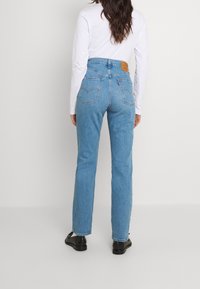 Ljusblå denimjeans med hög midja, femfickorsdesign och en läderpatch på baksidan. Passformen är rak med lätt spänning i tyget.