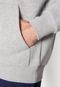 Grå sweatshirt med kengurulomme, ribbede manchetter og kant. Materialet virker blødt og tekstureret med et let meleret mønster.