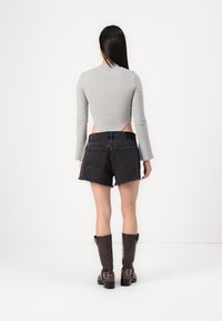 Harmaa ribattu pitkähihaisuus yläosa, jossa on avoin selkä, yhdistettynä mustiin denim-shortseihin, joissa on revitty helma ja taskut. Ruskeat polvipituiset saappaat.