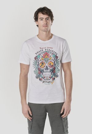 Camiseta blanca de manga corta con un gráfico colorido de calavera con elementos florales y tropicales. El texto incluye "Verano Tropical" y "Paraíso de Playa".