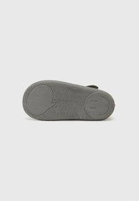 Grön slide sandal med en texturerad grå sula som har ett mönster av smileys. Ovandelen har en öppen design för ventilation och komfort.