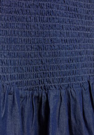 Nahaufnahme eines blauen Stoffes mit dicht zusammengezogenen Raffungnähten über lockeren, herabhängenden Falten.