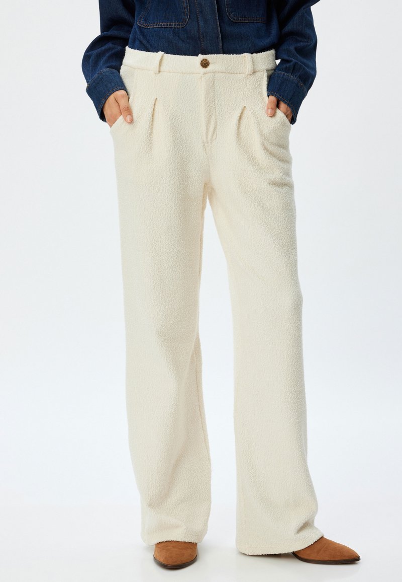 Pantalones de forro polar color crema con una superficie texturizada, de pierna ancha y con pliegues delanteros. Presentan un cierre de botón y bolsillos laterales.