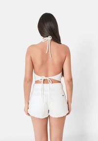 Witte haltertop van textuurstof met een open rug en striksluiting. Gecombineerd met hoge witte denimshorts met rafelige randen.