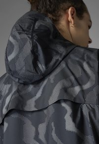 Schwarze Jacke mit einem geometrischen Punktemuster in Silber. Strukturierten Kapuze, geschichtetes Kragen-Design und elegante Nahtdetails für einen modernen Look.