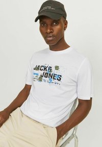 Camiseta de algodón blanca con un diseño gráfico en negro y varios colores que dice "JACK & JONES". Mangas cortas, cuello redondo, textura suave.