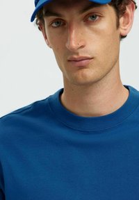 Blå bomulds t-shirt med rund hals, der har en glat tekstur og minimalistisk design. Kombineret med en blå cap.