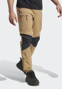 Beige outdoor pants with black accents and a side pocket, made of lightweight material. Elastic cuffs and reinforced knees enhance durability.