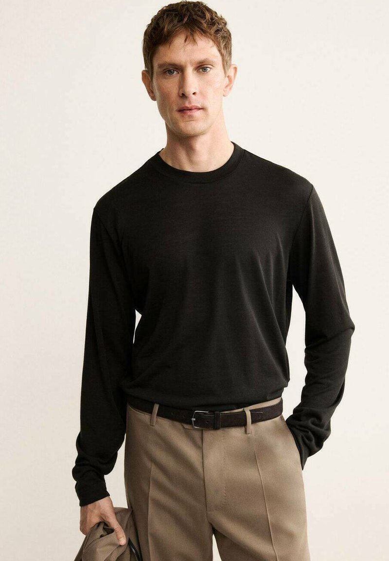 Black long-sleeve t-shirt made of lightweight material, featuring a round neckline and fitted cuffs, paired with beige trousers and a belt.