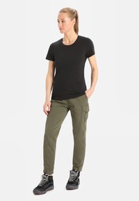 T-shirt nera a maniche corte abbinata a pantaloni cargo verde oliva. I pantaloni presentano tasche laterali e una vestibilità affusolata. Stivali neri con dettagli grigi.