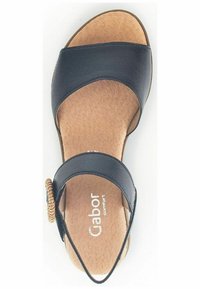 Sandale en cuir noir avec une large sangle sur le pied, un accent tressé circulaire sur le côté et une semelle intérieure rembourrée de couleur beige.