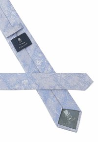 Hellblaues Fliegenband mit filigranen, weißen Blumenmustern, ausgestattet mit einem strukturierten Stoff und einem dunkelblauen Etikett mit Logo.