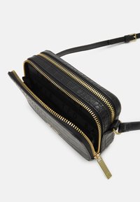 Sac en cuir noir à porter en bandoulière avec une texture crocodile, doté de deux compartiments zippés et de quincaillerie en ton or. Sangle réglable incluse.