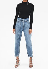 Top nero a costine a maniche lunghe abbinato a jeans denim azzurri a vita alta con cintura in vita e risvolti arrotolati. Sandali con tacco trasparente.