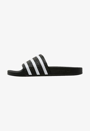 Sandalia tipo slide negra de Adidas con una tira texturizada que presenta tres rayas blancas y suela plana, vista lateral.
