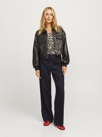 Svart faux lær bomberjakke med to brystlommer, kombinert med en topp med leopardmønster, mørke vide jeans og røde nettinghæler.