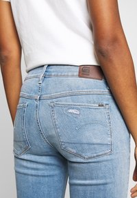 Jeans de mezclilla de color azul claro con un ajuste clásico. Incluyen un parche de logo de cuero marrón, un desgastado sutil y dos bolsillos traseros.