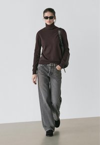 Bordeaux coltrui, grijze wijde jeans, zwarte schoenen en een zonnebril. Eenvoudig ontwerp met een zachte textuur en een ontspannen silhouet.