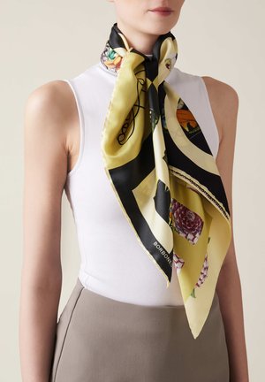 La sciarpa di seta presenta un design giallo e nero con motivi floreali e accenti geometrici. Indossata come una sciarpa per il collo per uno stile decorativo.