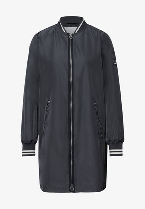 Lungo giubbotto bomber nero con zip frontale intera color argento, due tasche laterali con zip, polsini e colletto a coste con strisce bianche e una toppa sulla manica sinistra.