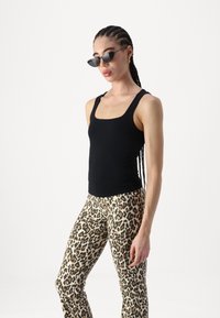 Crna uska majica bez rukava s kvadratnim izrezom, uparena s hlačama u leopard uzorku koje se šire prema dolje. Dodatci uključuju crne mačkaste sunčane naočale.